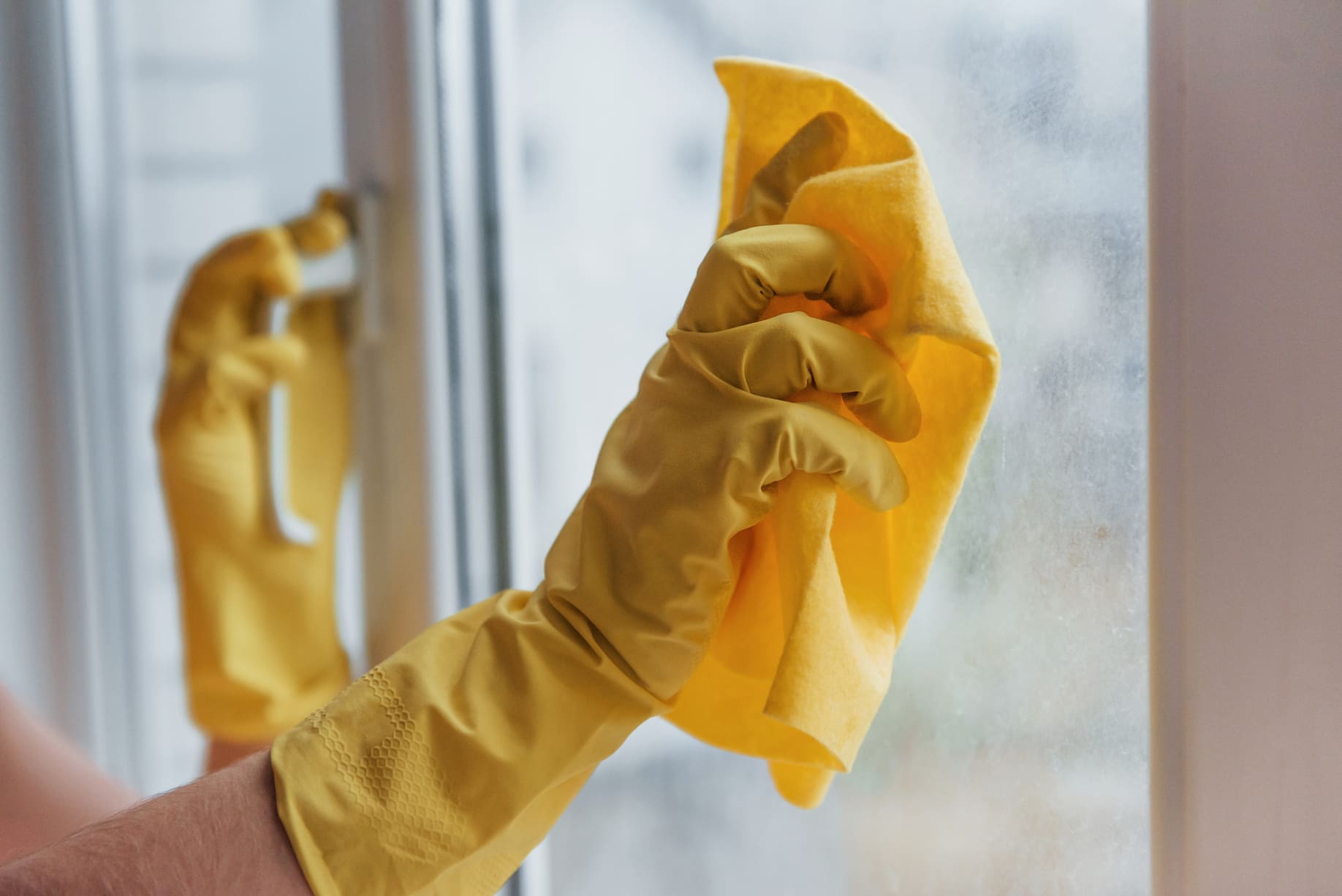 Manos limpiando una ventana con un paño amarillo.